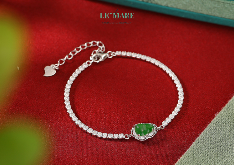 Lấy cảm hứng từ vẻ đẹp thuần khiết của ngọc bích và sự cát tường của hồ lô, chiếc vòng tay bạc nữ Thanh Lô được chế tác tỉ mỉ từ bạc cao cấp, điểm xuyết viên ngọc bích xanh biếc hình hồ lô – biểu tượng phong thủy của sự trường thọ, hạnh phúc và tài lộc. Thiết kế tinh giản, mềm mại nhưng đầy cuốn hút, Thanh Lô như một vầng sương nhẹ quấn quanh cổ tay, khơi dậy vẻ duyên dáng và sang trọng tự nhiên của người phụ nữ.Không cầu kỳ, không rườm rà, nhưng chiếc vòng tay ấy vẫn đủ khiến người đối diện không thể rời mắt. Vì bên trong nó là sự hòa quyện tinh tế giữa thẩm mỹ và tâm linh – một món trang sức mang linh khí, như một lá bùa hộ mệnh ẩn chứa thông điệp của sự may mắn và viên mãn.